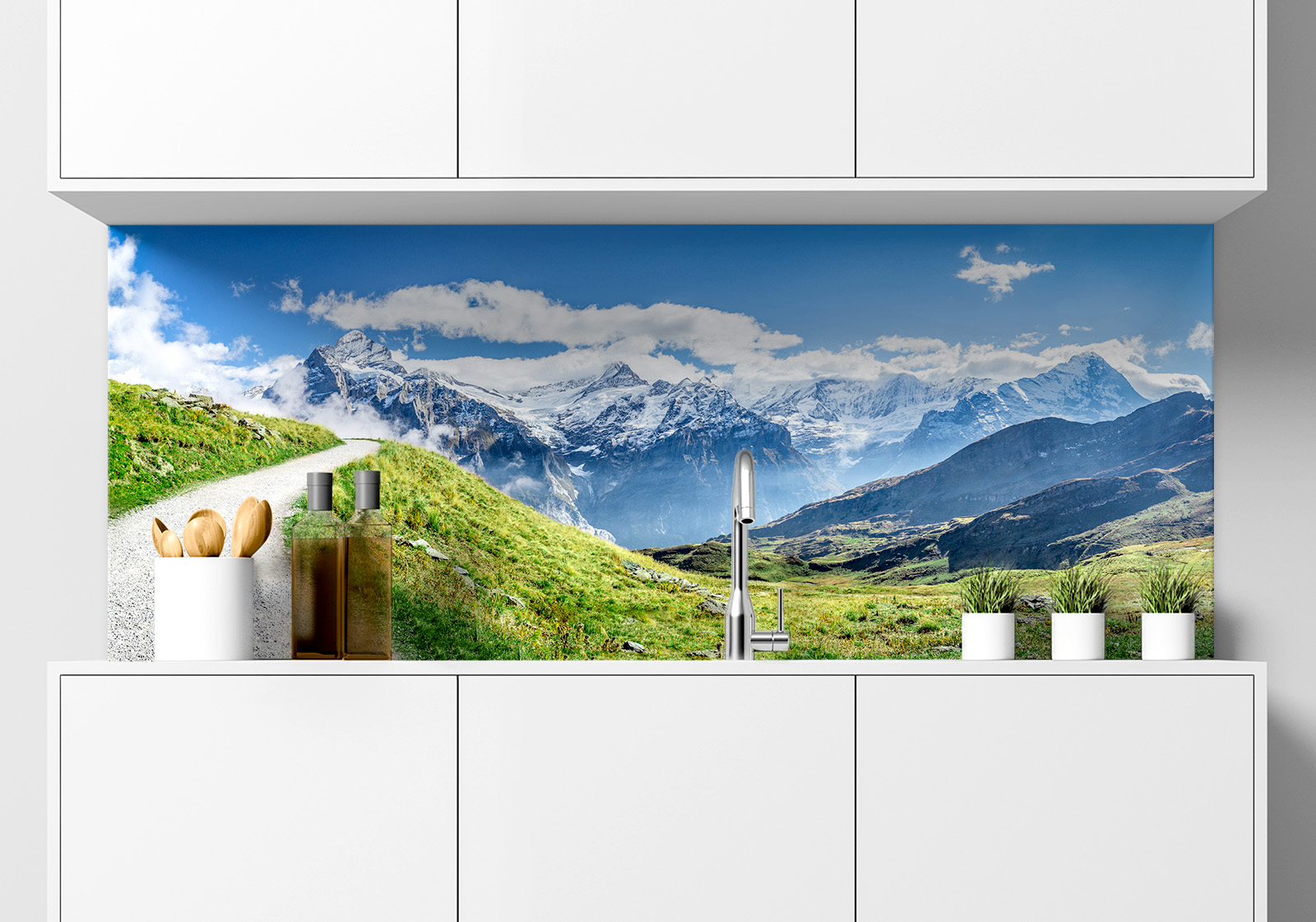 Küchenrückwand - Alpen Berge Küche  mit weißen Hängeschränken, Spüle, Gewürzständer, Topfpflanzen und Küchenrückwand mit folgendem Motiv: Wanderweg durch grüne Wiesen in den Schweizer Alpen, mit Blick auf schneebedeckte Berggipfel und blauen Himmel mit Wolken.