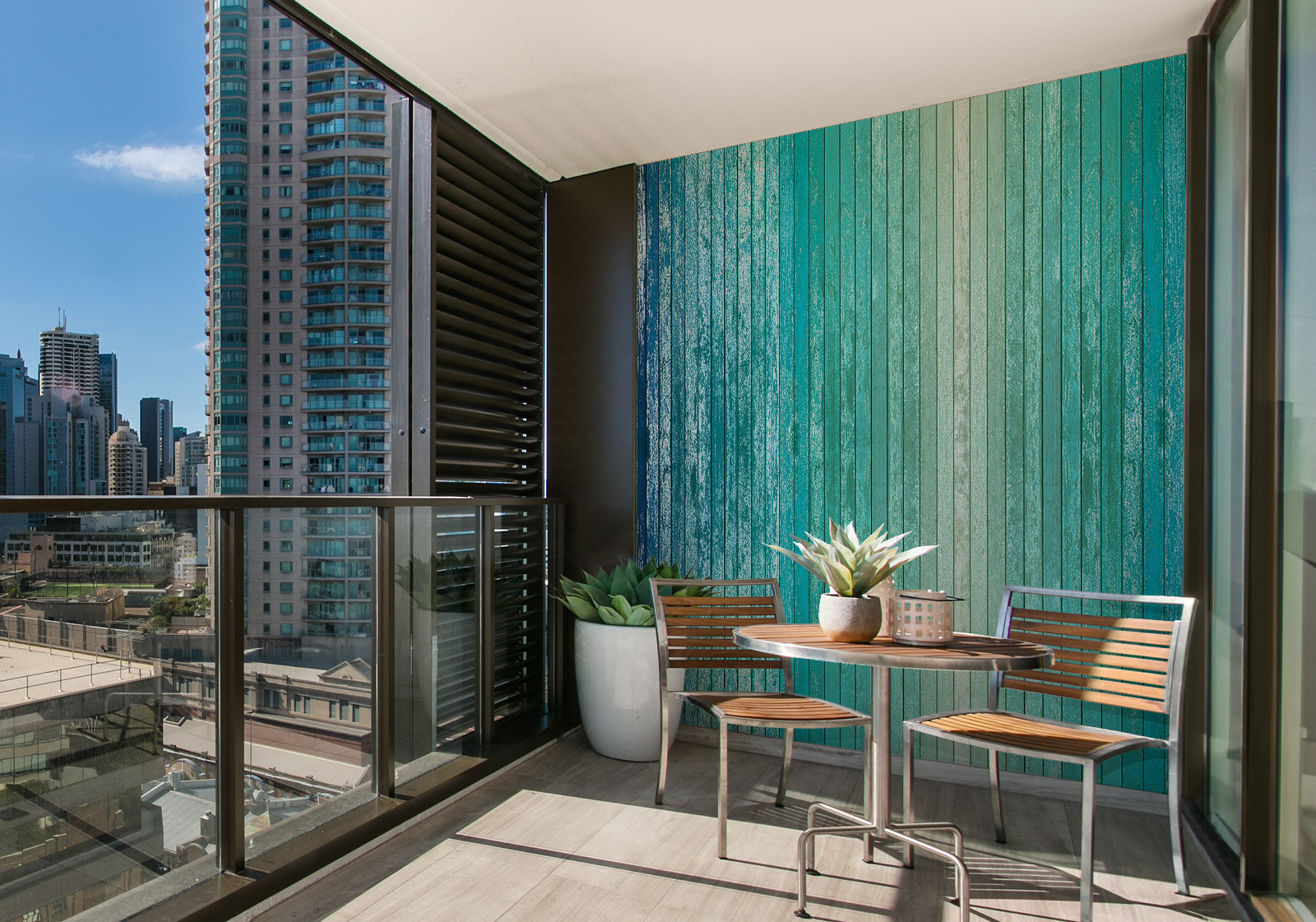 Milieubild mit Balkon mit Tisch und Stühlen, mit  Blick auf die Stad  und einer Wandverkleidung mit folgendem Motiv: Holzplanken in Farbverlauf von Beige über Türkis bis Dunkelblau, mit sichtbarer Maserung und leichtem Vintage-Effekt.