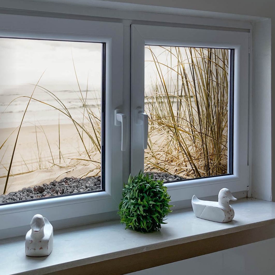 Lichtschachtbild konfigurieren! Zwei Fenster mit einem Lichtschacht und Topfpflanze und zwei Entenfiguren auf der Fensterban. Im Lichtschacht ist ein Lichtschachtbild platziert mit folgendem Motiv: Strandhafer im Sand, Meer im Hintergrund, bewölkter Himmel.