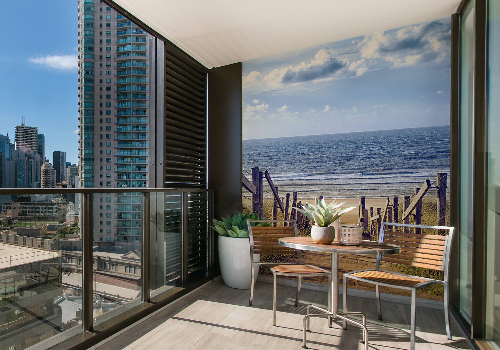 Milieubild mit Balkon mit Tisch und Stühlen, mit  Blick auf die Stadt und einer Wandverkleidung mit folgendem Motiv: Weg mit Holzgeländer führt durch Dünen zum Sandstrand mit Blick auf Meer und Wellen.
