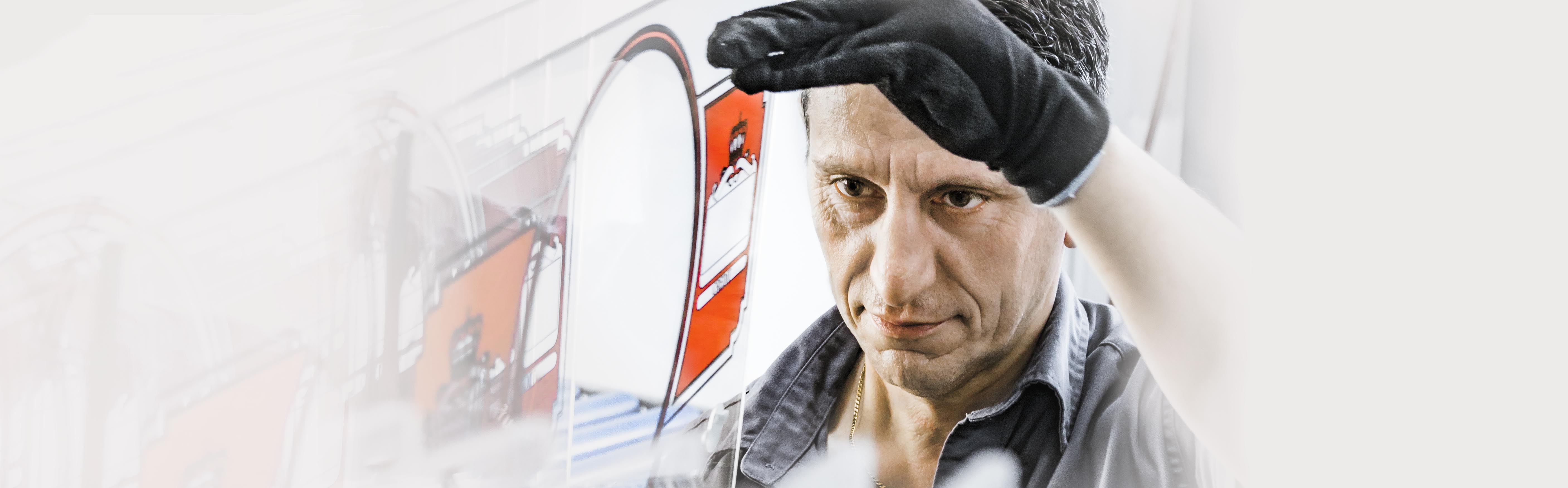Mann mit schwarzem Handschuh arbeitet an einer bedruckten Platte. Nahaufnahme seines Gesichts und der Hand während er die Platte in der Hand hält und die Qualität begutachtet.