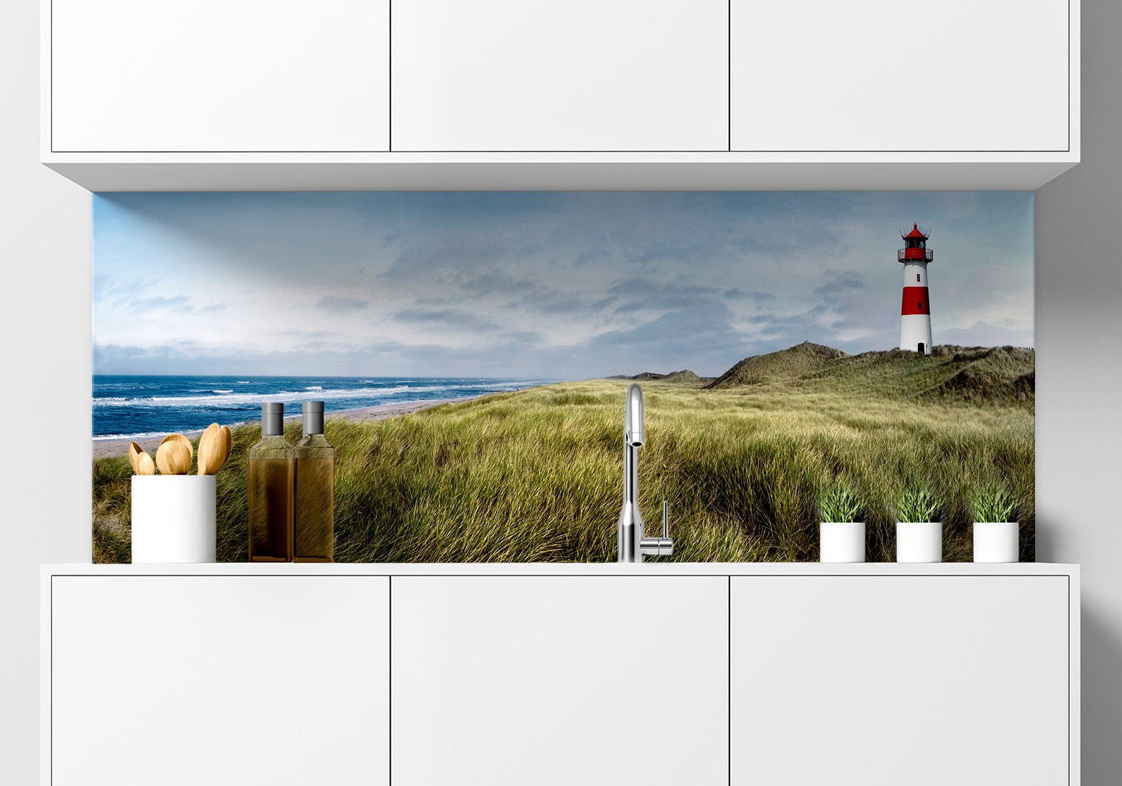 Küchenrückwand -  Leuchtturm auf Sylt mit Strand Küche mit weißen Hängeschränken, Spüle mit Armatur, Gewürzständer und kleinen Topfpflanzen auf der Arbeitsfläche. Es ist eine Küchenrückwand mit folgendem Motiv verbaut: Panoramablick auf Strand mit Dünengras, Meer und Leuchtturm, bewölkter Himmel.