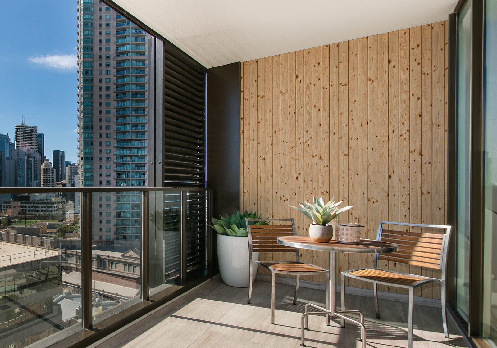 Milieubild mit Balkon mit Tisch und Stühlen, mit  Blick auf die Stad  und einer Wandverkleidung mit folgendem Motiv: Helle Holzplanken mit sichtbarer Maserung und Astlöchern, vertikal angeordnet.