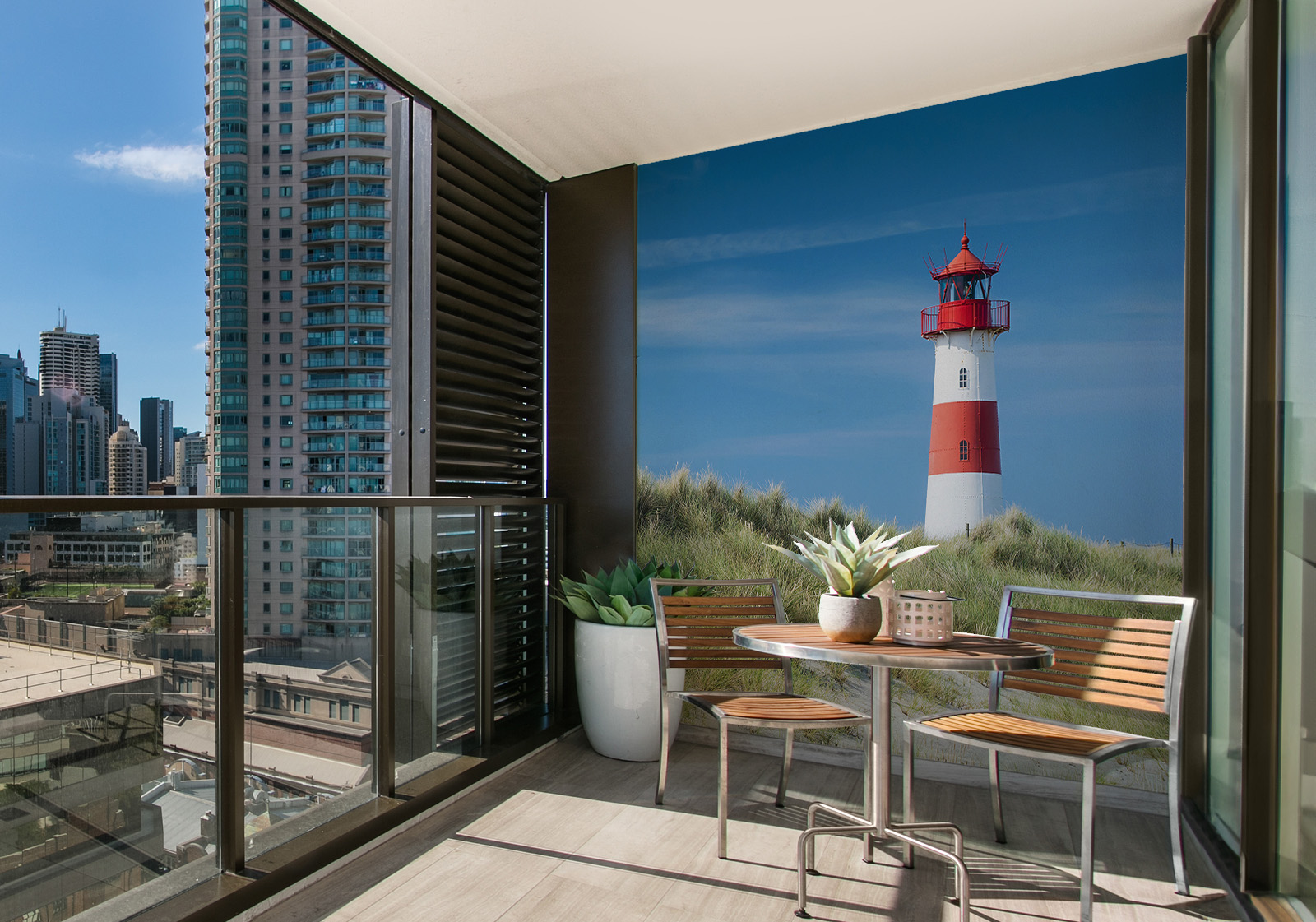 Wandverkleidung für den Außenbereich mit Motiv Leuchtturm auf Sylt Nordsee Milieubild mit Balkon mit Tisch und Stühlen, mit  Blick auf die Stad  und einer Wandverkleidung mit folgendem Motiv: Leuchtturm in rot und weiß vor blauem Himmel, im Vordergrund Dünen mit Dünengras und Zaun.