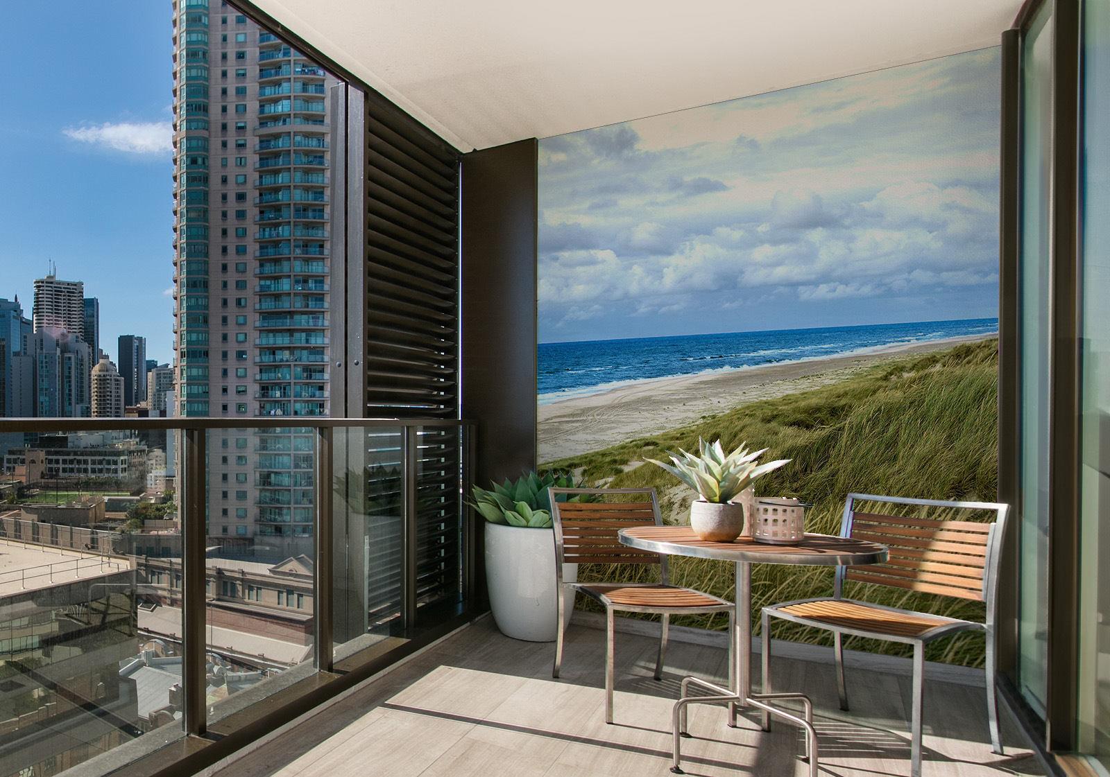 Milieubild mit Balkon mit Tisch und Stühlen, mit  Blick auf die Stad  und einer Wandverkleidung mit folgendem Motiv: Panoramablick auf Strand mit Dünengras, Meer und Leuchtturm, bewölkter Himmel.