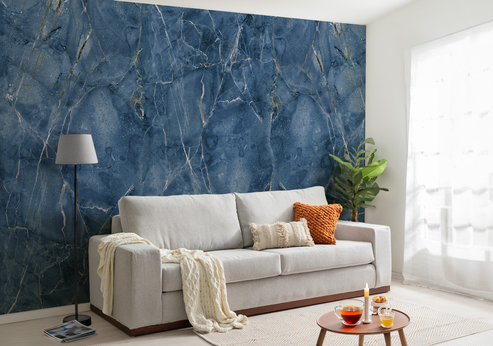 Milieubild mit Wohnzimmer mit grauer Couch, Zierkissen, Decke, Beistelltisch, Lampe, Pflanze und einer Wandverkleidung mit folgendem Motiv: Dunkelblauer Marmor mit goldenen und weißen Adern, abstrakte Textur.