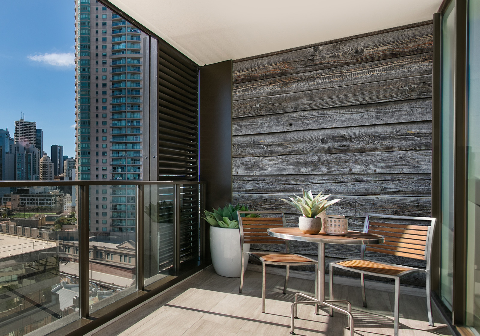 Milieubild mit Balkon mit Tisch und Stühlen, mit  Blick auf die Stad  und einer Wandverkleidung mit folgendem Motiv: Graue Holzplanken mit sichtbarer Maserung, symmetrisch angeordnet.