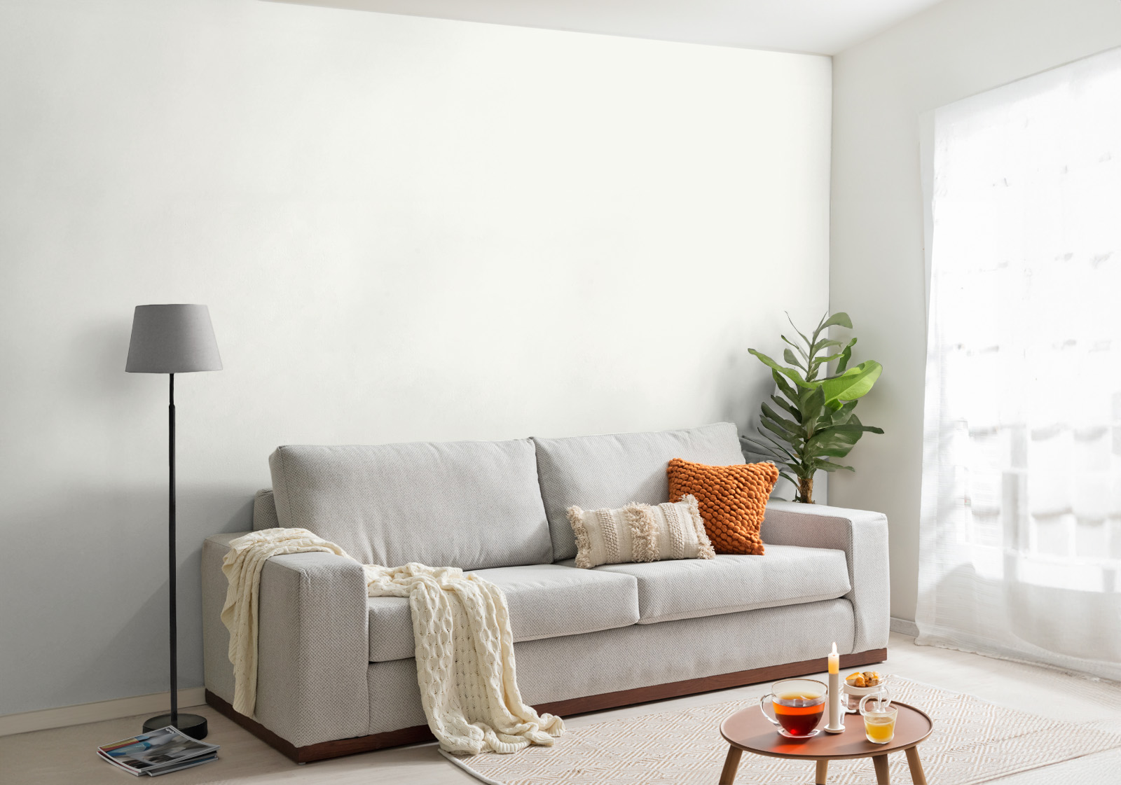 Milieubild mit Wohnzimmer mit grauer Couch, Zierkissen, Decke, Beistelltisch, Lampe, Pflanze und einer Wandverkleidung mit folgendem Motiv: Einfarbig weißes Bild, keine sichtbaren Details oder Muster.