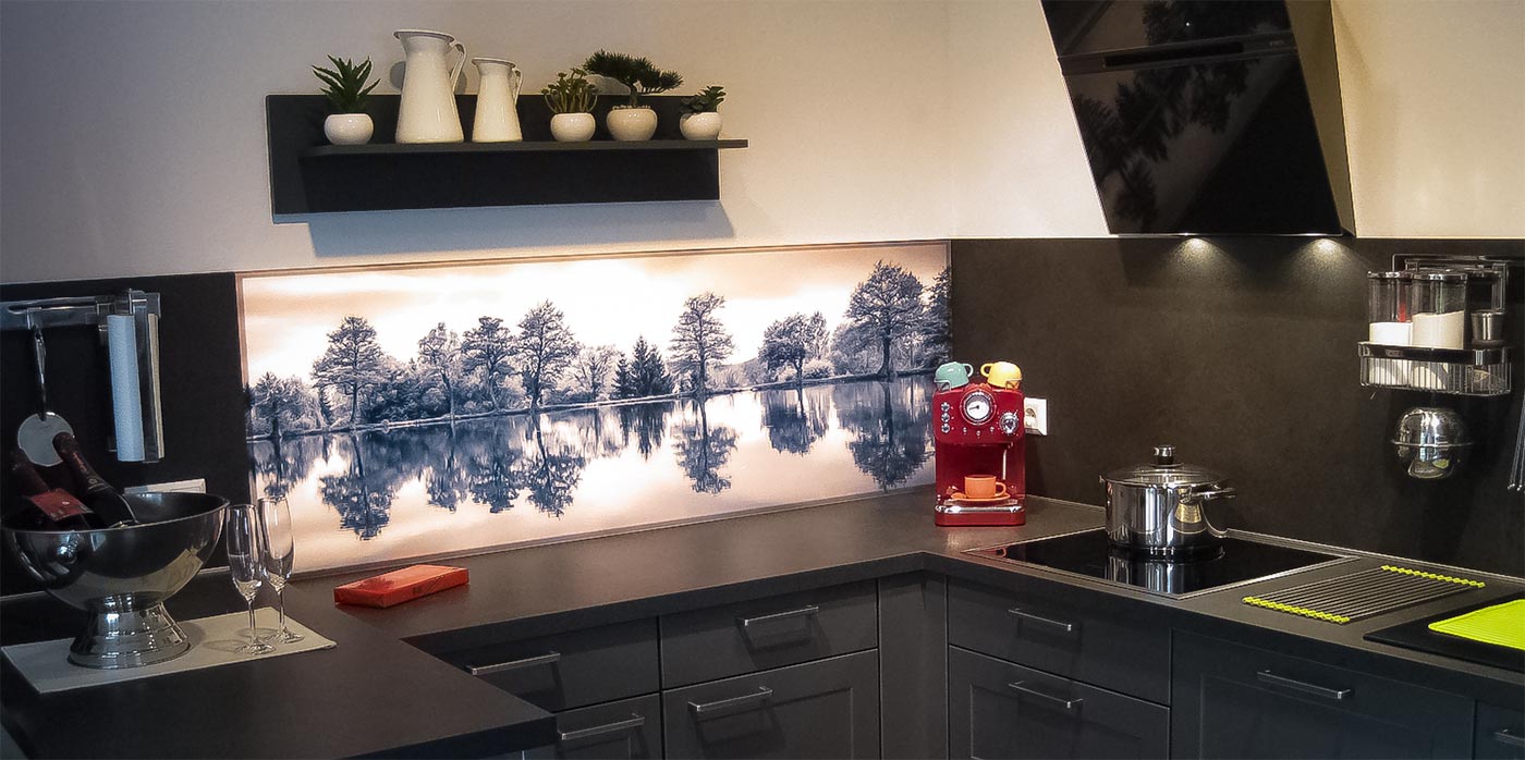 Modern eingerichtete Küche mit grauen Unterschränken, schwarzer Arbeitsplatte, einer roten Kaffeemaschine und einem Wandbild mit See.