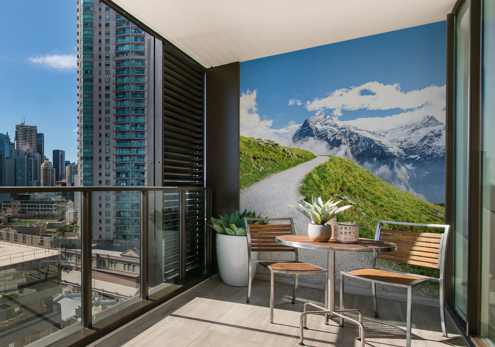 Wandverkleidung für den Außenbereich mit Motiv Alpen Berge Milieubild mit Balkon mit Tisch und Stühlen, mit  Blick auf die Stad  und einer Wandverkleidung mit folgendem Motiv: Wanderweg durch grüne Wiesen in den Schweizer Alpen, mit Blick auf schneebedeckte Berggipfel und blauen Himmel mit Wolken.