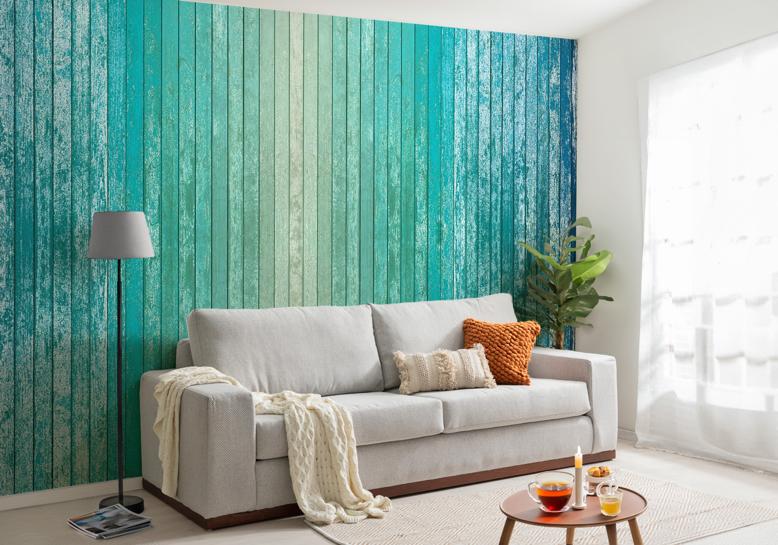 Milieubild mit Wohnzimmer, grauer Couch, Zierkissen, Decke, Beistelltisch, Lampe, Pflanze und einer Wandverkleidung mit folgendem Motiv: Holzplanken in Farbverlauf von Beige über Türkis bis Dunkelblau, mit sichtbarer Maserung und leichtem Vintage-Effekt.