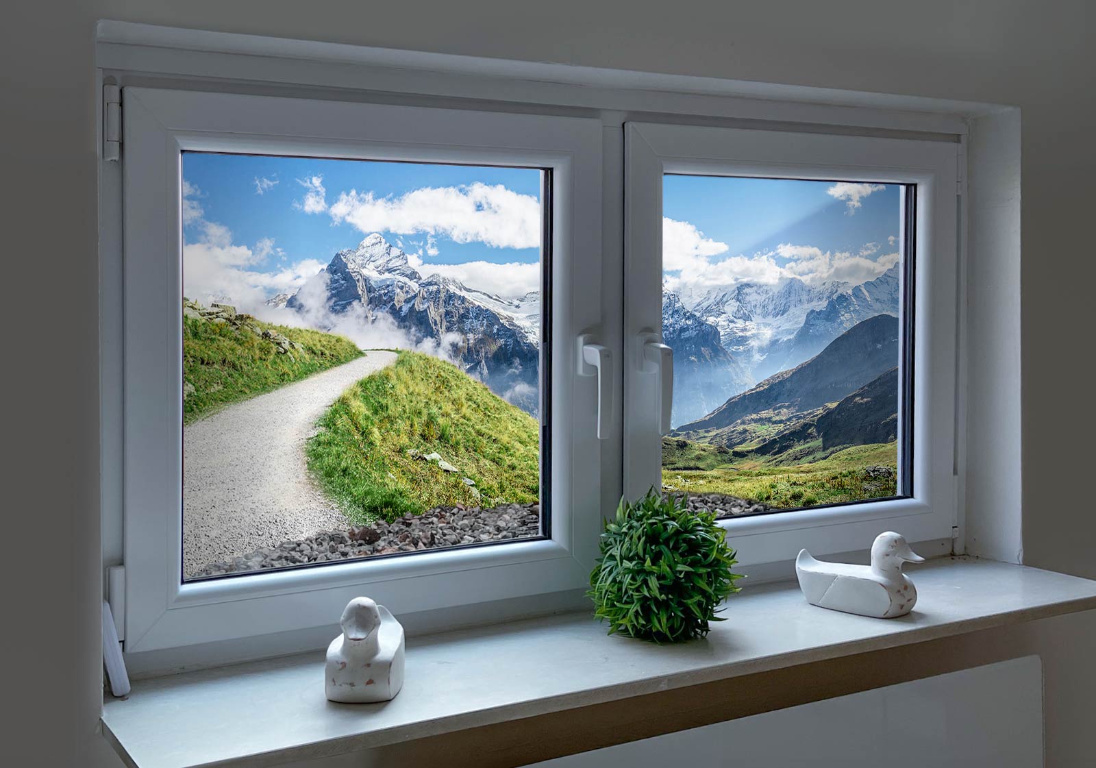Hier klicken und entdecken Lichtschachtfenster mit Topfpflanze, zwei Entenfiguren auf der Fensterbank. Außen ein Lichtschachtbil mit folgendem Motiv: Wanderweg durch grüne Wiesen in den Schweizer Alpen, mit Blick auf schneebedeckte Berggipfel und blauen Himmel mit Wolken.