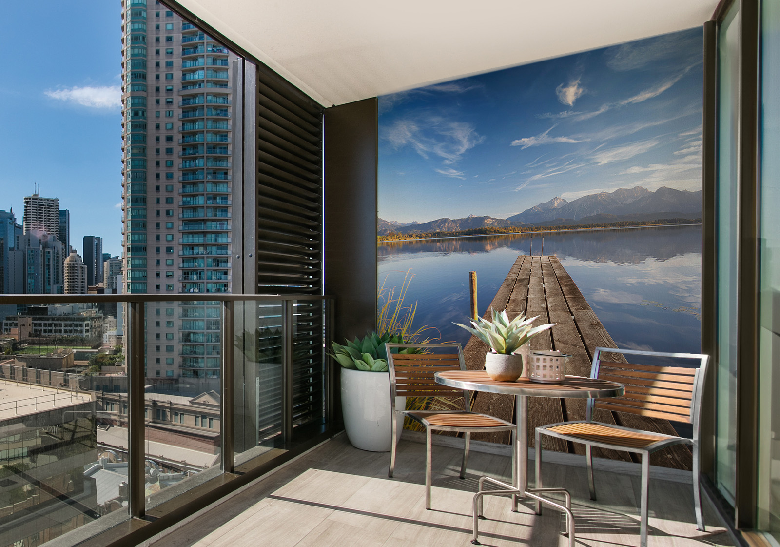 Milieubild mit Balkon mit Tisch und Stühlen, mit  Blick auf die Stadt und einer Wandverkleidung mit folgendem Motiv: Holzsteg am Badesee mit im Wasser spiegelndem Bergpanorama, seitlich hohe Wassergräser.