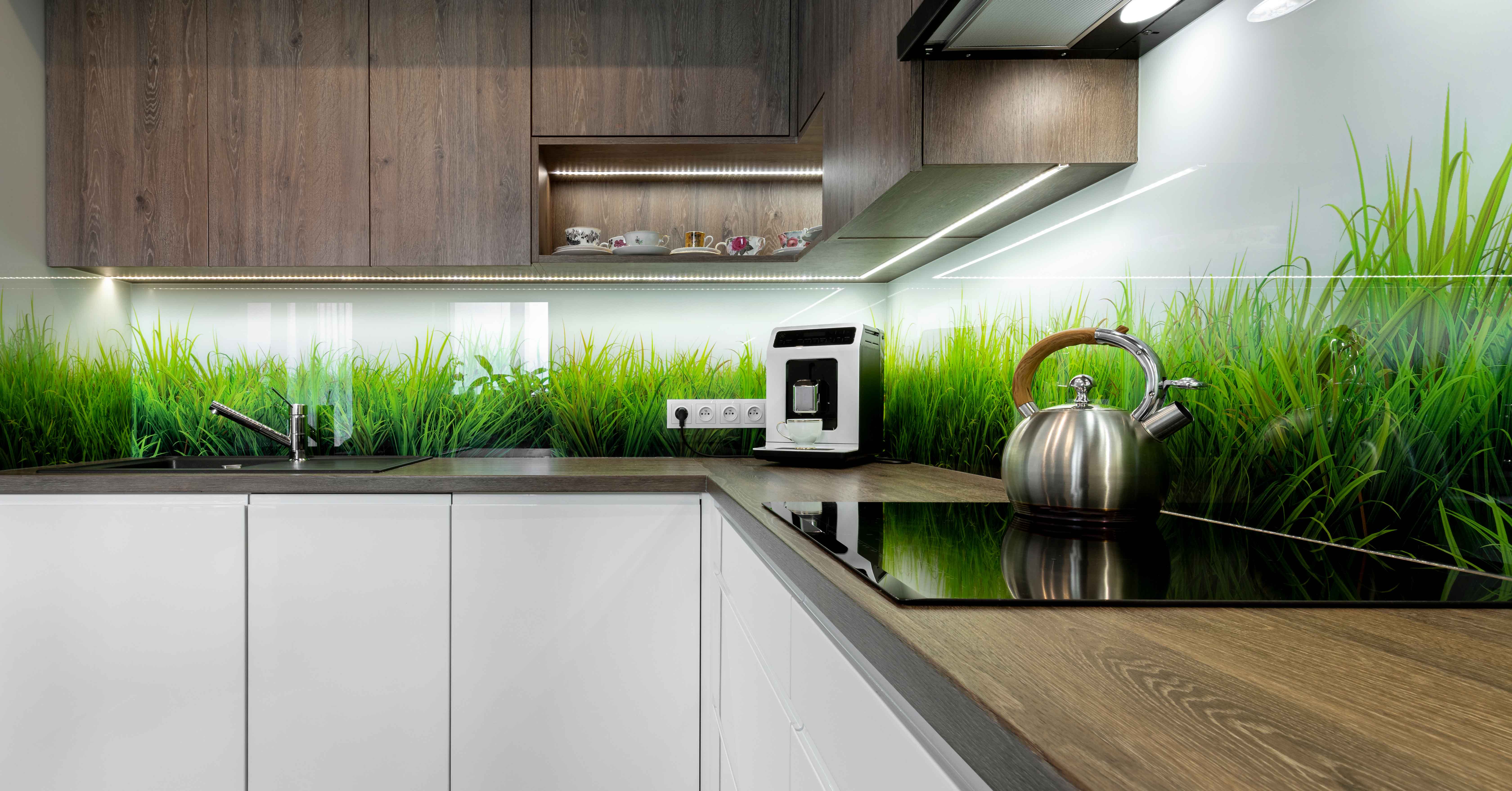 Moderne Küche mit Holz- und Weißfronten, Glasküchenrückwand mit Grasmotiv, Wasserkocher, Kaffeemaschine und Unterbau-LED-Beleuchtung.