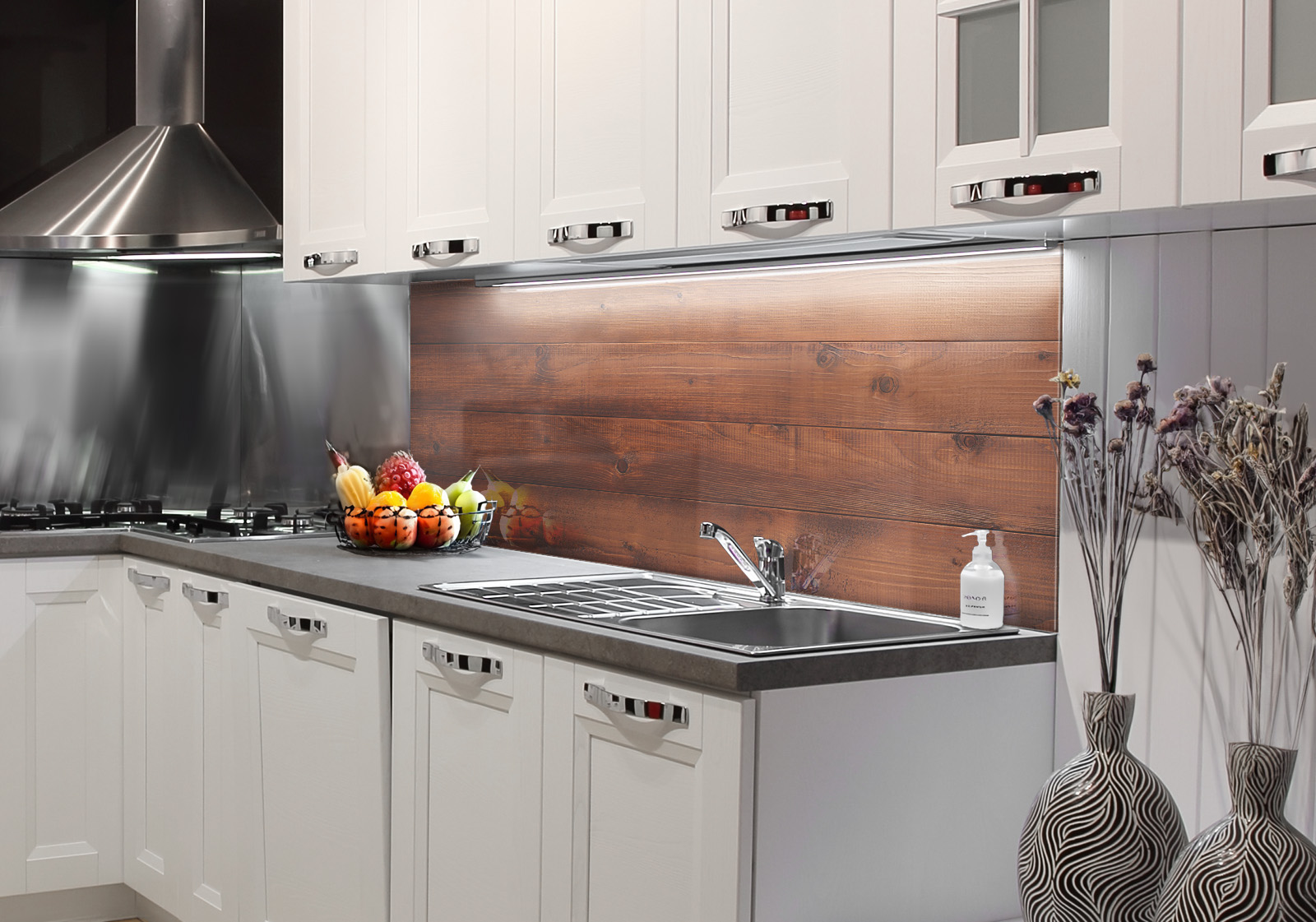 Weiße Küche mit Edelstahl-Dunstabzugshaube, Spüle, Obstschale und zwei Vasen mit Dekozweigen. Es ist eine Küchenrückwand mit folgendem Motiv verbaut: Dunkelbraune Holzplanken mit sichtbarer Maserung, horizontal angeordnet und symmetrisch gespiegelt.