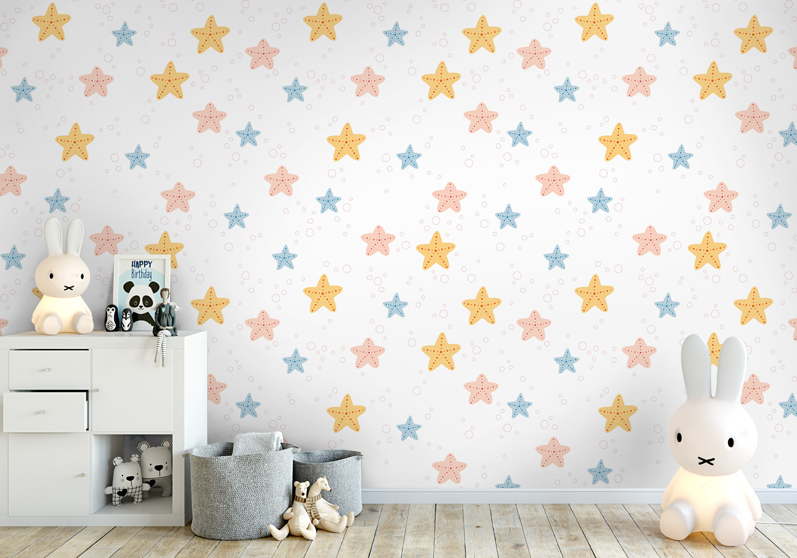 Wandverkleidung für das Kinderzimmer - buntes Seesternmuster Milieubild mit  Kinderzimmer mit weißer Kommode, Hasenlampe, Spielzeug, grauen Körben auf dem Boden und einer Wandverkleidung mit folgendem Motiv: Muster mit gelben, rosa und blauen Seesternen und kleinen Blasen auf weißem Hintergrund.