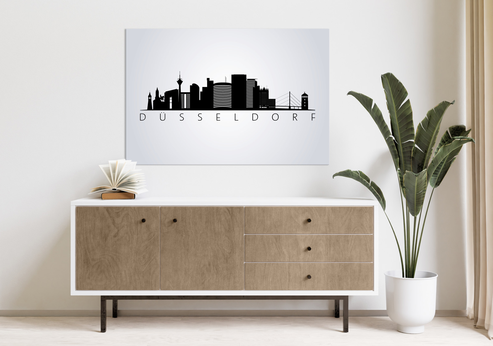 Milieubild mit hellem Holzsideboard mit Pflanze und darüber ein Wandbild mit folgendem Motiv: Silhouette der Düsseldorfer Skyline auf grauem Hintergrund, darunter der Schriftzug "DÜSSELDORF".