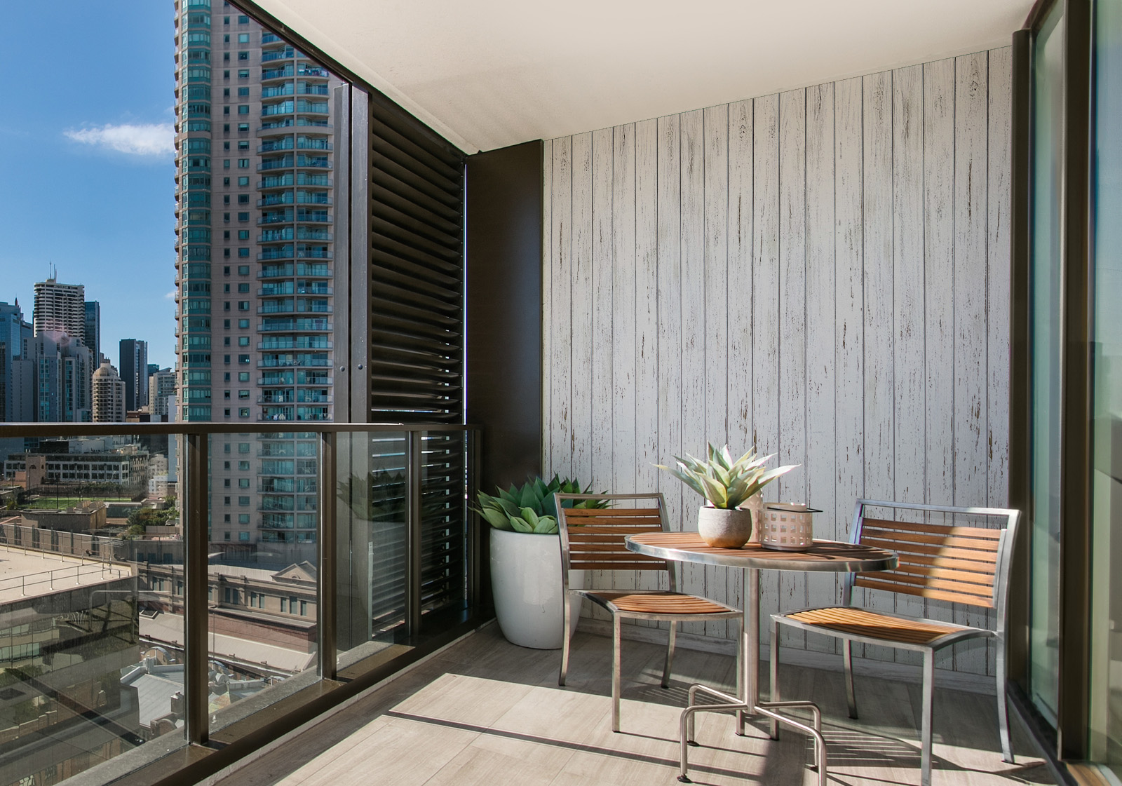 Wandverkleidung für den Außenbereich - weißes Holz Milieubild mit Balkon mit Tisch und Stühlen, mit  Blick auf die Stad  und einer Wandverkleidung mit folgendem Motiv: Weiße Holzplanken mit leichter Maserung, vertikal angeordnet und leichtem Vintage-Effekt.