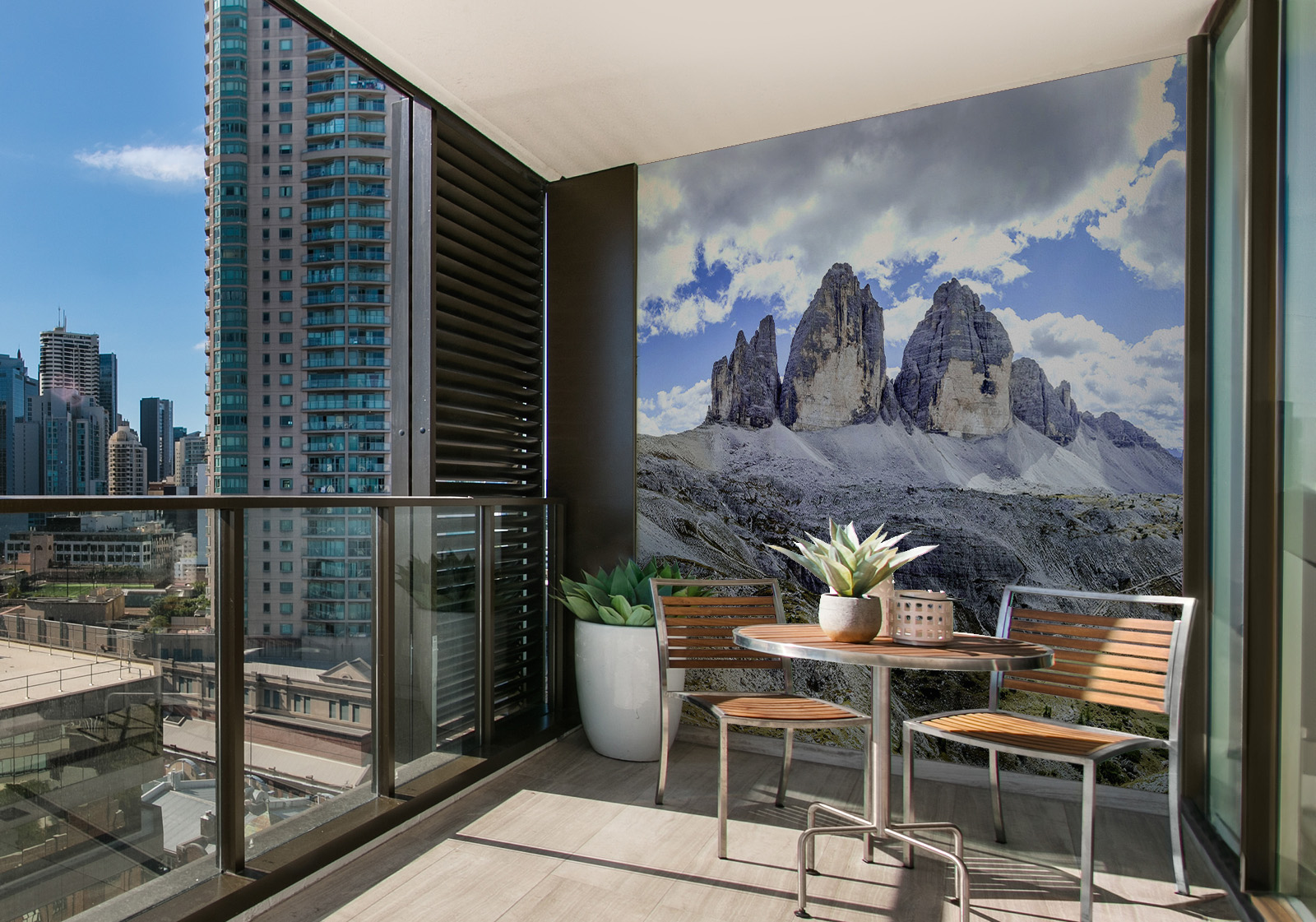 Milieubild mit Balkon mit Tisch und Stühlen, mit  Blick auf die Stad  und einer Wandverkleidung mit folgendem Motiv: Panorama der zerklüfteten Gipfel der Dolomiten unter einem Himmel mit flauschigen Wolken, mit einem kleinen See in einem Tal.