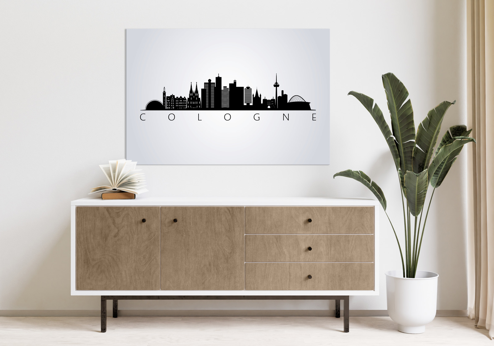 Milieubild mit hellem Holzsideboard mit Pflanze und darüber ein Wandbild mit folgendem Motiv: Silhouette der Kölner Skyline auf grauem Hintergrund, darunter der Schriftzug "COLOGNE".