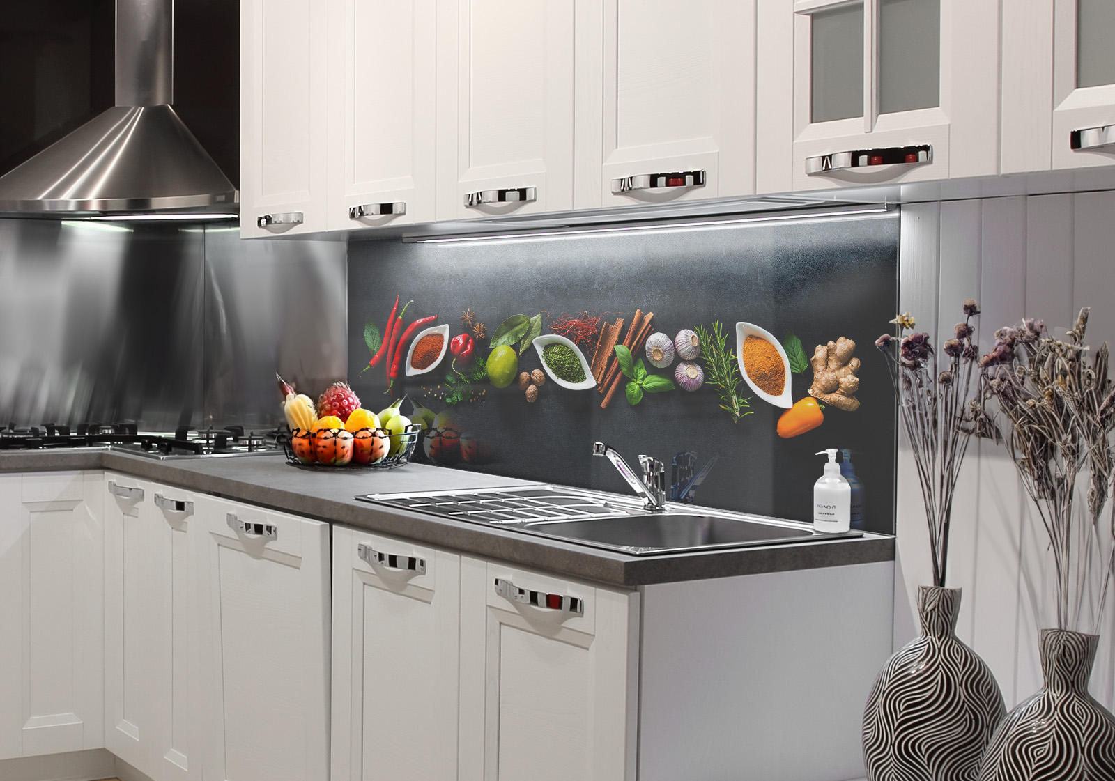RW-K-P_Gewürze-02.jpg Weiße Küche mit  Edelstahl-Dunstabzugshaube, Spüle, Obstschale und zwei Vasen mit Dekozweigen und Küchenrückwand mit Motiv: Verschiedene Gewürze und Kräuter in weißen Schalen auf einem dunklen, strukturierten Untergrund, von oben fotografiert.